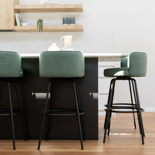 Green upholstered swivel bar stool with black metal legs positioned beside a modern timber kitchen counter.